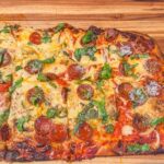 Pizza in teglia dorata, alta e soffice, pronta da sfornare con ingredienti freschi.