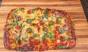 Pizza in teglia dorata, alta e soffice, pronta da sfornare con ingredienti freschi.