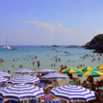 Spiaggia sabbiosa italiana con ombrelloni colorati e turisti felici in cerca di vacanze economiche.