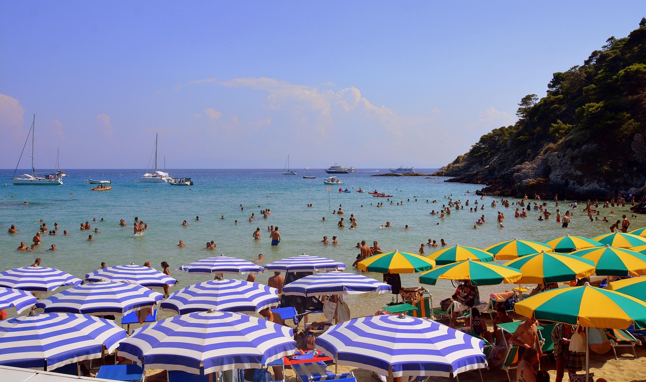Spiaggia sabbiosa italiana con ombrelloni colorati e turisti felici in cerca di vacanze economiche.